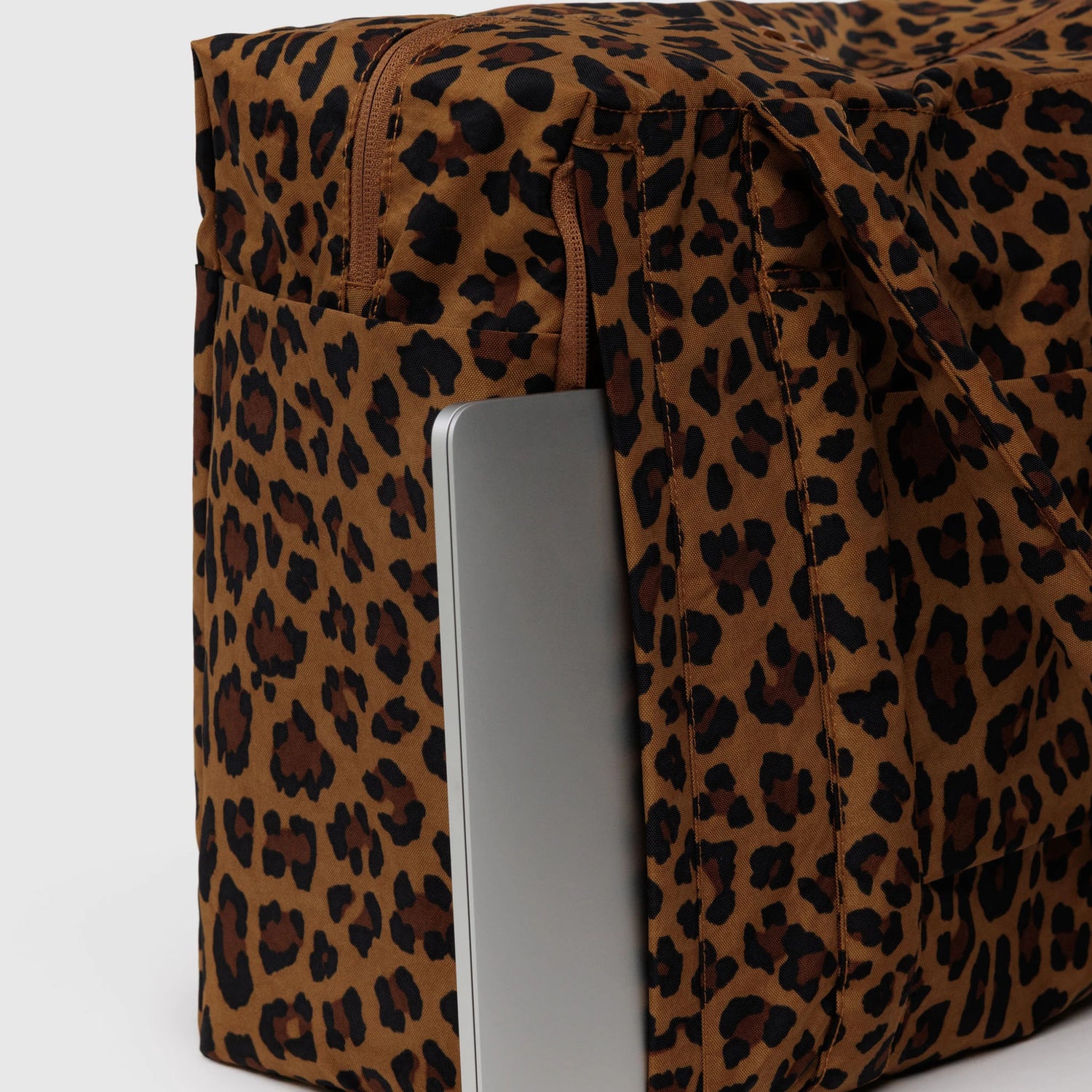 Close-up of the Baggu Small Cloud Carry-on - Leopard by Baggu, featuring a laptop partially in the side pocket—a lightweight, stylish travel bag for your essentials.
