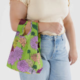 A person holds a chic Baby Baggu Reusable Bag in the Dahlia pattern, perfectly complementing their beige top and blue jeans.