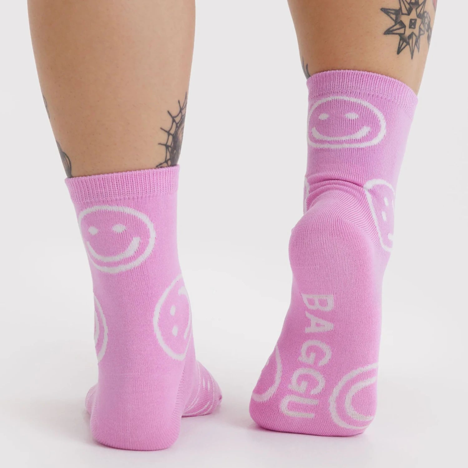 Pair of mid-calf pink socks featuring white smiley faces and white text on sole against a plain white background