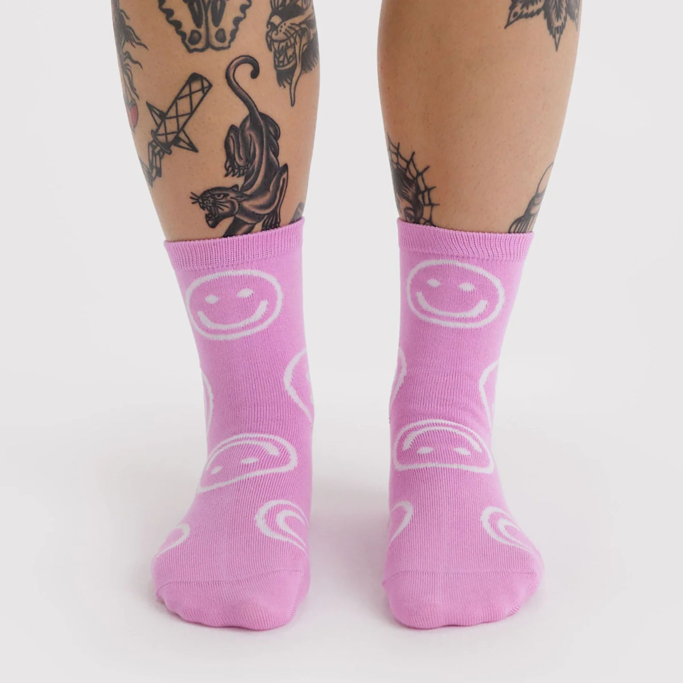 Pair of light purple crew socks decorated with large white smiley faces worn on feet against a white background