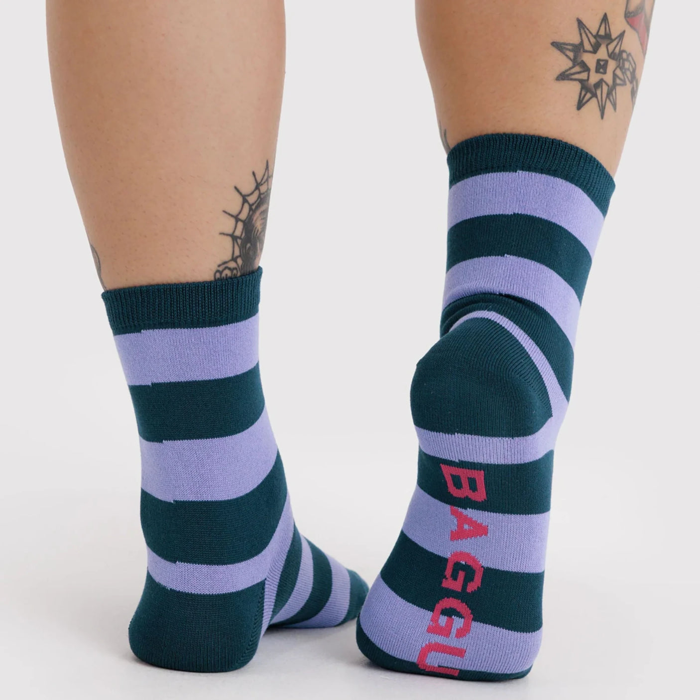 Pair of mid-calf socks with wide navy and lavender horizontal stripes, red text on sole, worn on feet against white background