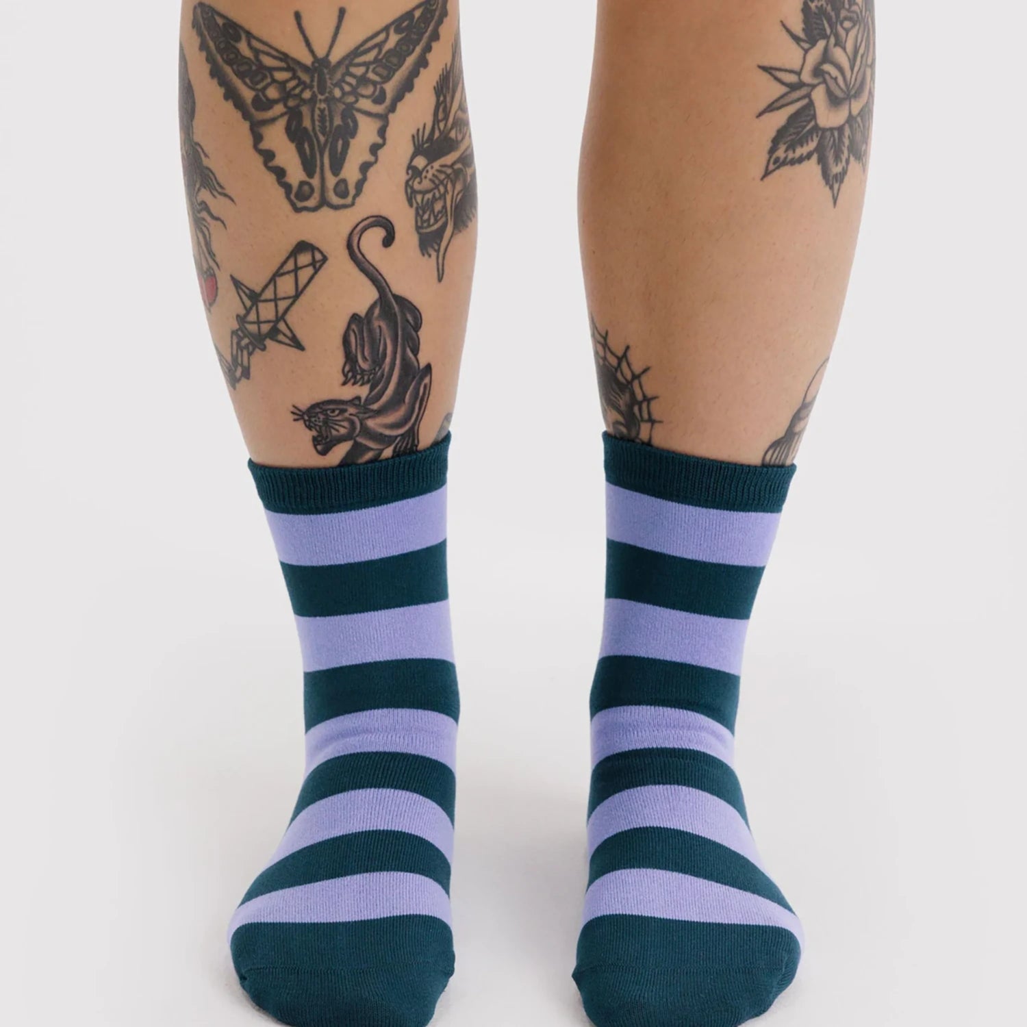 Pair of crew socks with alternating thick navy blue and lavender horizontal stripes worn on feet against white background