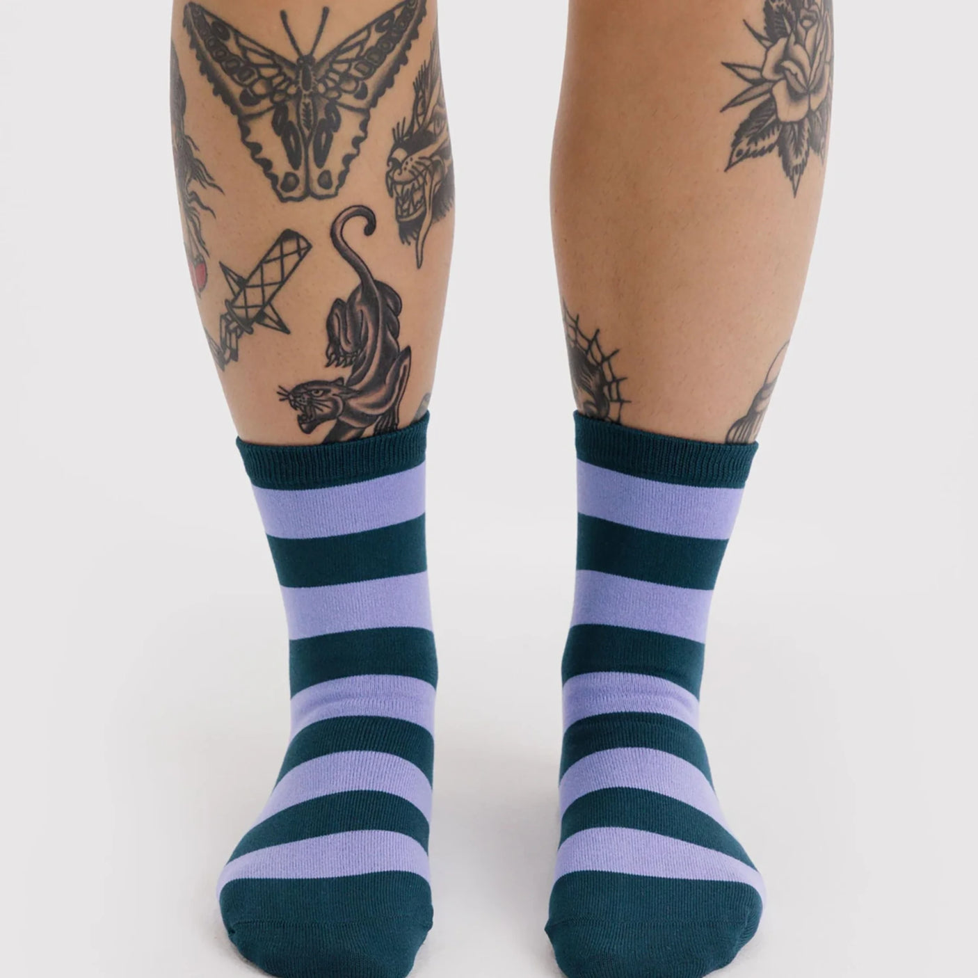 Pair of crew socks with alternating thick navy blue and lavender horizontal stripes worn on feet against white background