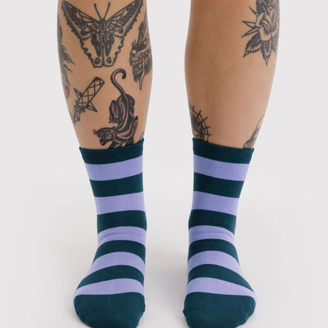 Pair of crew socks with alternating thick navy blue and lavender horizontal stripes worn on feet against white background
