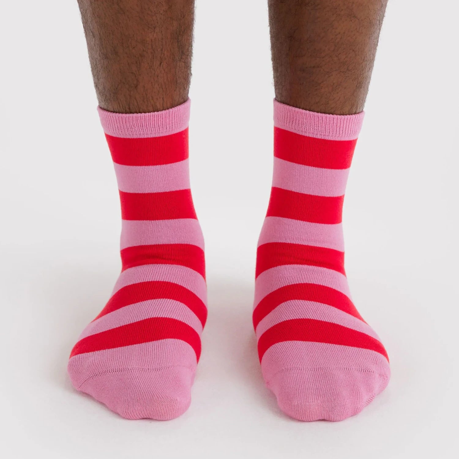 Pair of crew socks featuring bold horizontal stripes in alternating pink and red worn on feet against white background