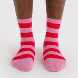 Pair of crew socks featuring bold horizontal stripes in alternating pink and red worn on feet against white background