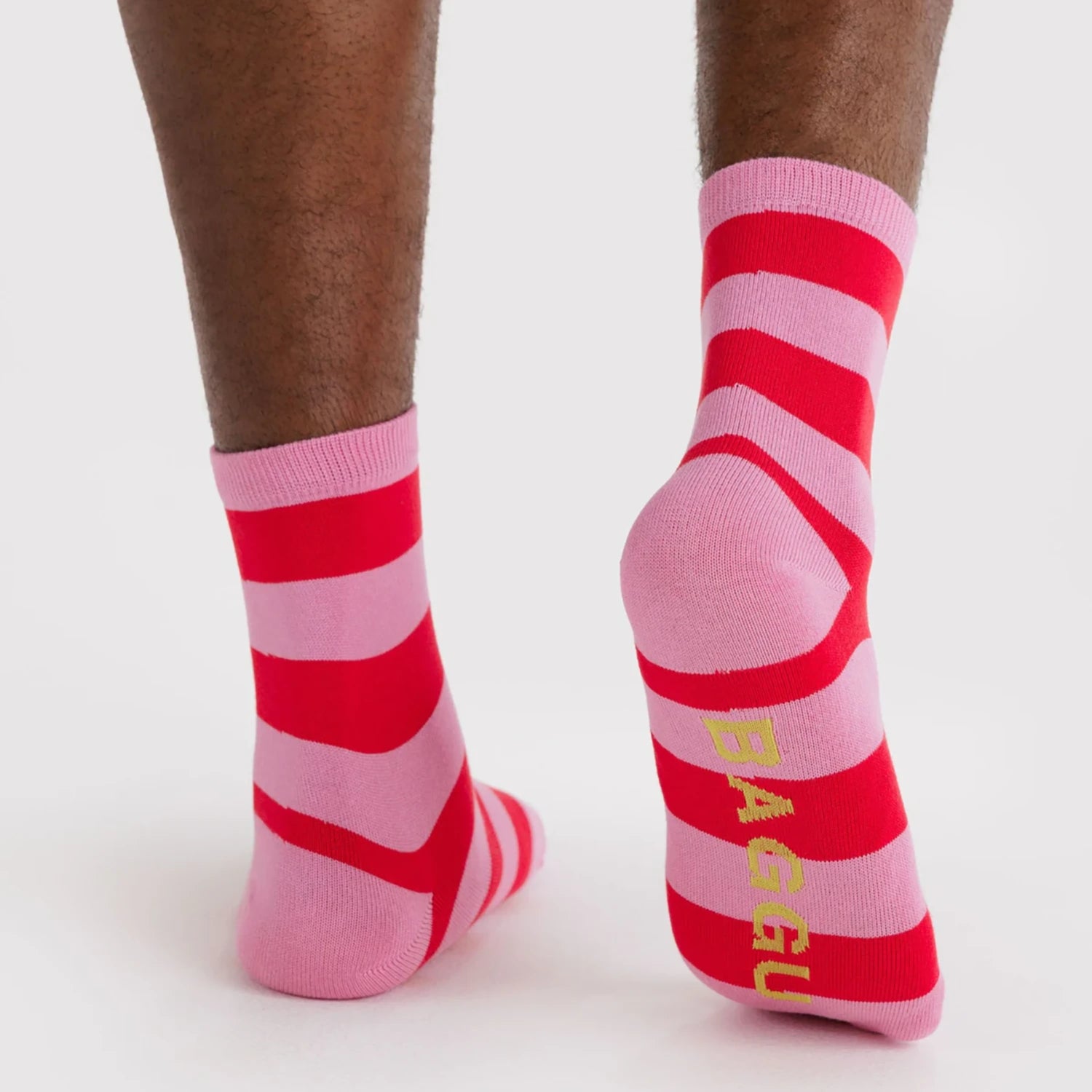 Pair of crew socks with wide horizontal red and pink stripes and yellow text on sole against plain background
