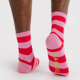 Pair of crew socks with wide horizontal red and pink stripes and yellow text on sole against plain background