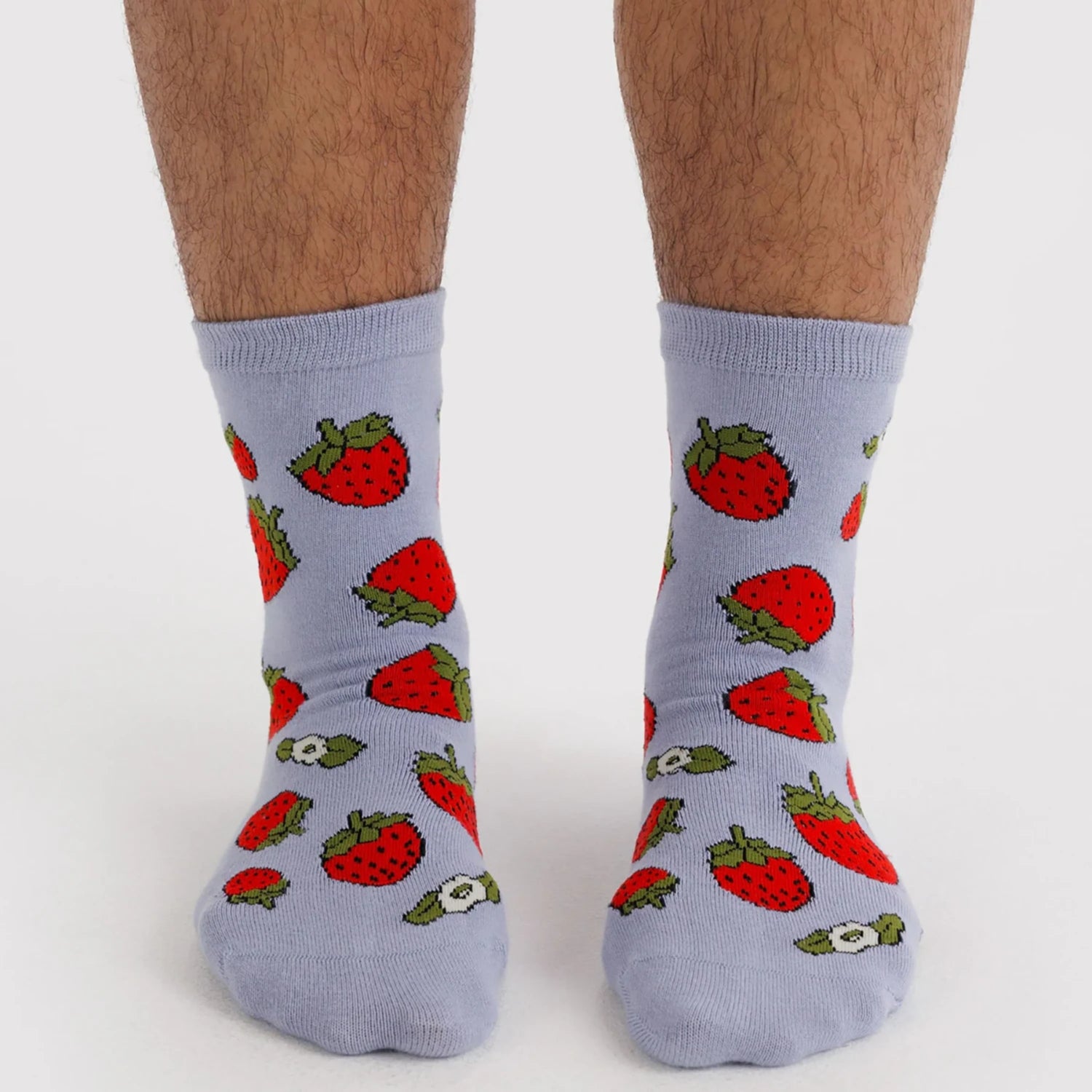 Pair of light gray crew socks adorned with bright red strawberries with green leaves on feet against a white background