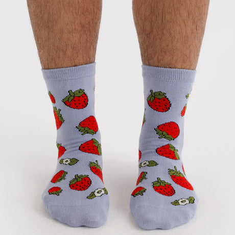 Pair of light gray crew socks adorned with bright red strawberries with green leaves on feet against a white background