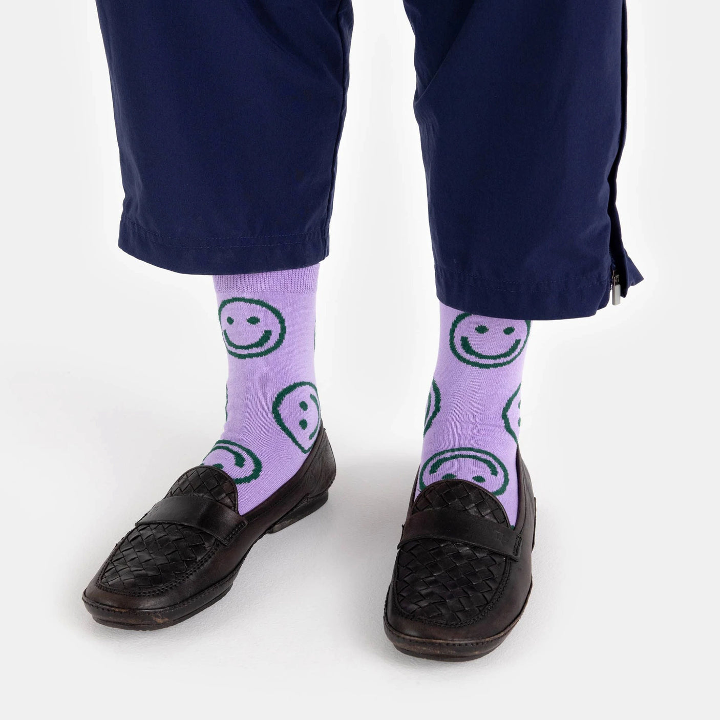 A person wears Baggu Crew Sock - Lavender Happy, navy pants, and black woven loafers.