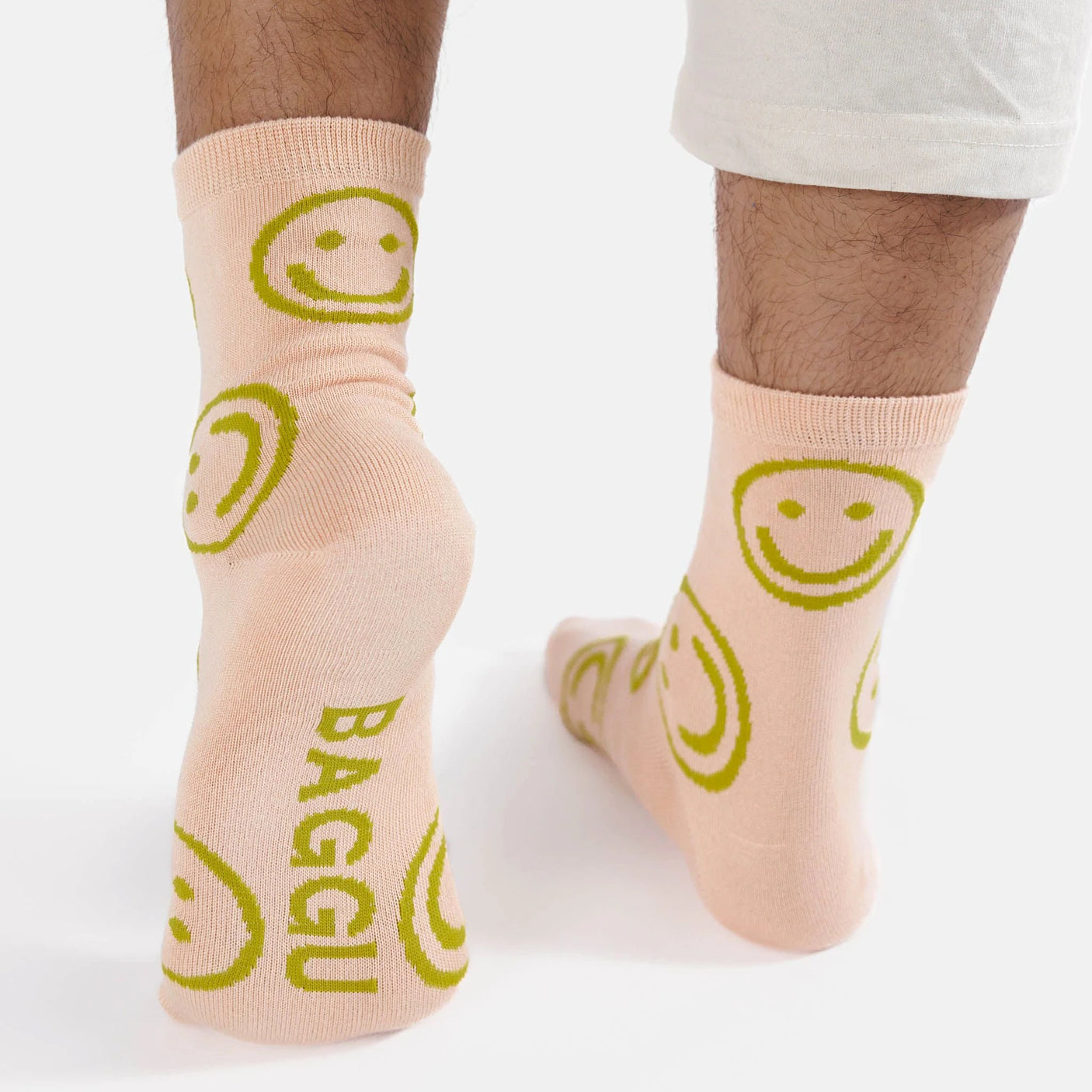 Two feet cozily wrapped in the Baggu Crew Sock - Light Pink Happy feature a soft fabric with green smiley faces and the word "BAGGU." Made by Baggu from bamboo rayon, these socks provide a gentle touch that’s sure to brighten your day.