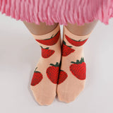 The Baggu Crew Sock - Strawberry, by Baggu, exudes charming strawberry vibes with its pink hue and delightful red strawberry patterns. Perfectly paired with a pleated pink skirt, these socks are crafted from soft bamboo rayon for comfort and style, offering a whimsical touch when viewed from above.