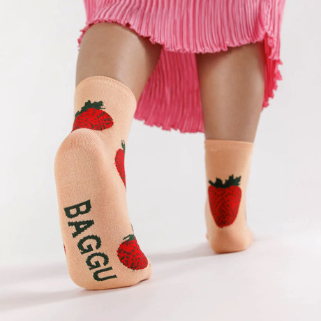 A person wearing Baggu Crew Sock - Strawberry by Baggu, with strawberry designs and a hint of bamboo rayon, paired perfectly with a pink pleated skirt creates ultimate strawberry vibes.