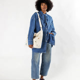 A person stylishly dressed in a denim outfit holds the Baggu Duck Bag Medium in Ditsy Floral against a plain background.