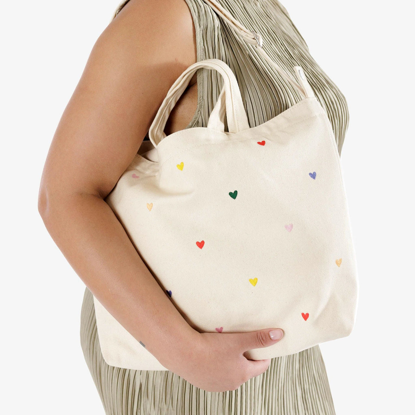 A person holding the Baggu Duck Bag Medium by Baggu, a cream-colored tote adorned with embroidered hearts and featuring a zip top closure for added security.