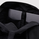 Interior view of black tote bag with padded compartment holding a laptop secured by a branded strap
