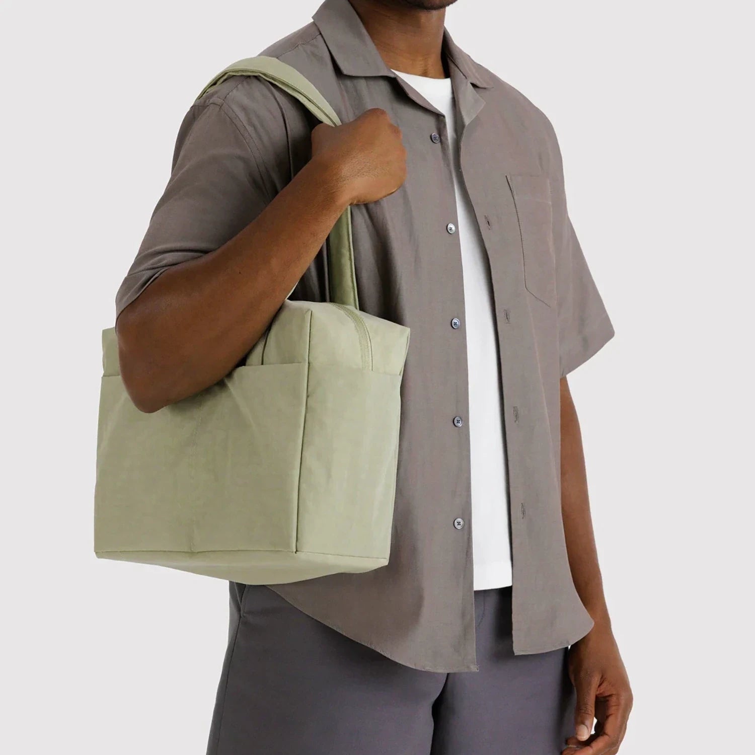 Man holding light green square tote bag with wide handles and exterior side pockets against plain background