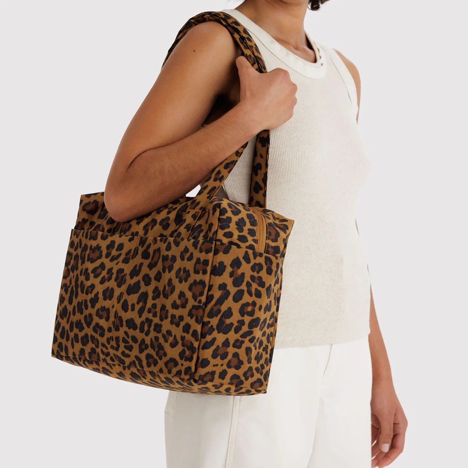 Woman holding large leopard print tote bag with two shoulder straps against neutral background