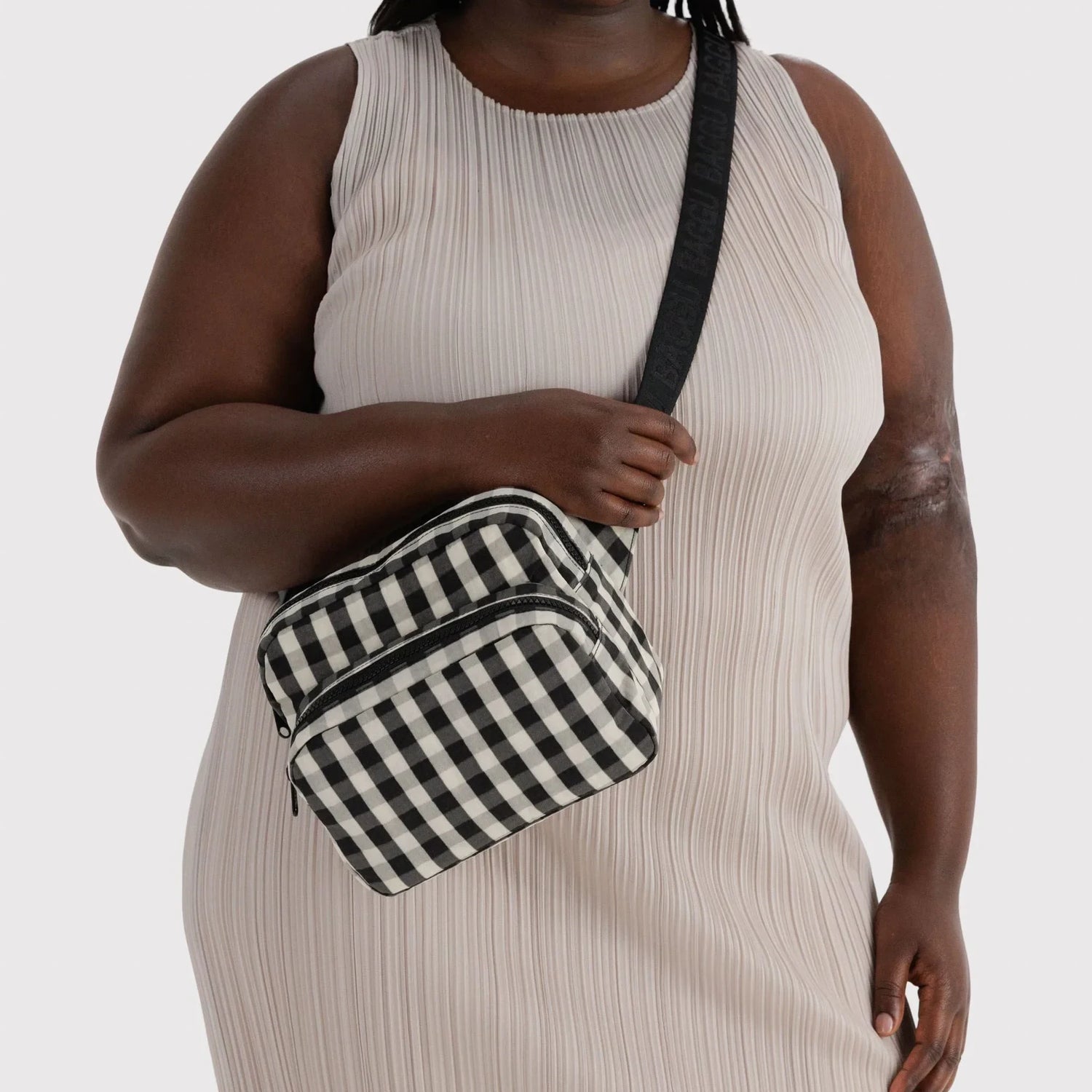 Baggu gingham fanny pack worn crossbody with black strap and zipper