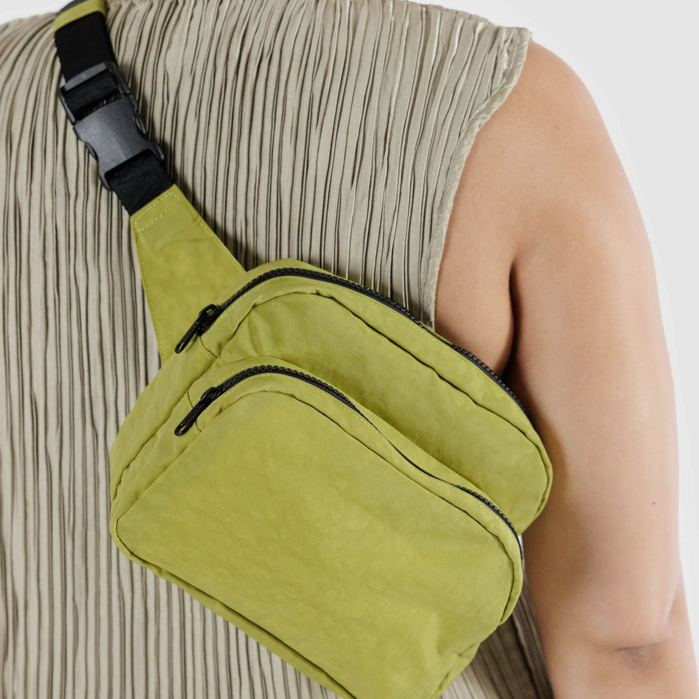 A person wearing a pleated sleeveless top and a Baggu Fanny Pack in lemongrass, featuring black zippers and an adjustable strap, showcasing eco-friendly style.