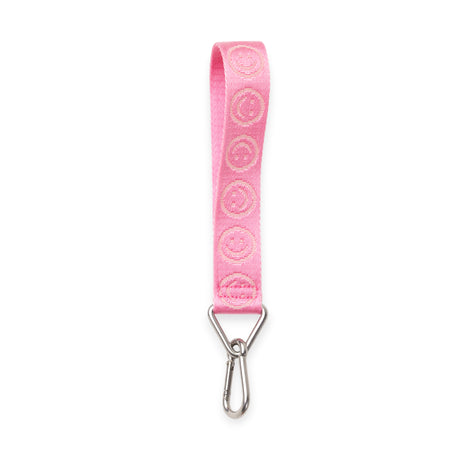 Pink fabric wrist strap with repeated smiley face embroidery and silver metal carabiner clip on white background