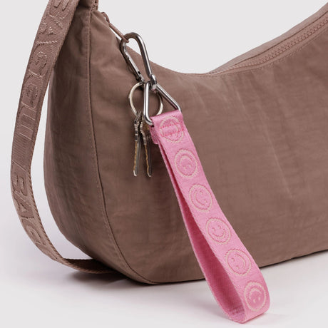 Baggu logo keychain strap in pink with metal rings attached to a brown bag