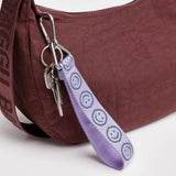 Lilac smiley logo keychain strap with silver clips, close-up attachment loop