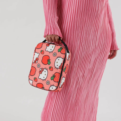 A person in a pink pleated dress holds the Hello Kitty x Baggu Lunch Bag, which features Hello Kitty and strawberry patterns and is crafted from recycled polyester.