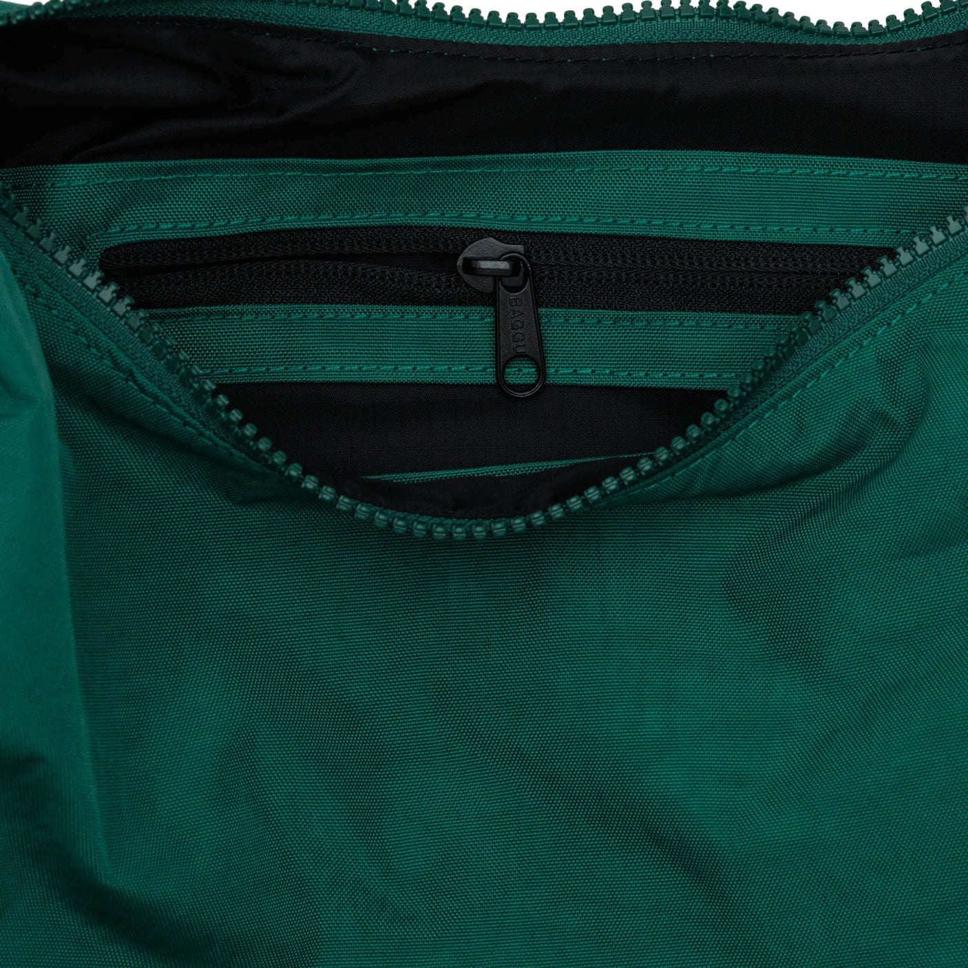 Close-up of an open Baggu Medium Nylon Crescent Bag in Cypress color, showcasing a black zippered pocket inside and an adjustable tonal logo strap.