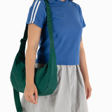 Person wearing a blue shirt and gray skirt, holding the Baggu Medium Nylon Crescent Bag in Cypress with an adjustable tonal logo strap.