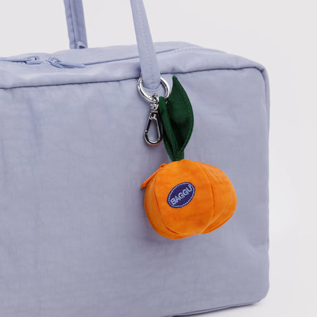 Orange plush fruit keychain with green leaf attached to light purple bag zipper pull loop