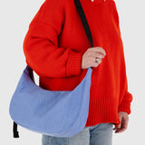 A person in a red sweater holds a Baggu Medium Nylon Crescent Bag - Cornflower by Baggu, crafted from recycled nylon, against a plain background.