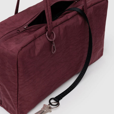 Close-up of mahogany Baggu medium nylon bowler bag with zipper open and black key leash attached to keys