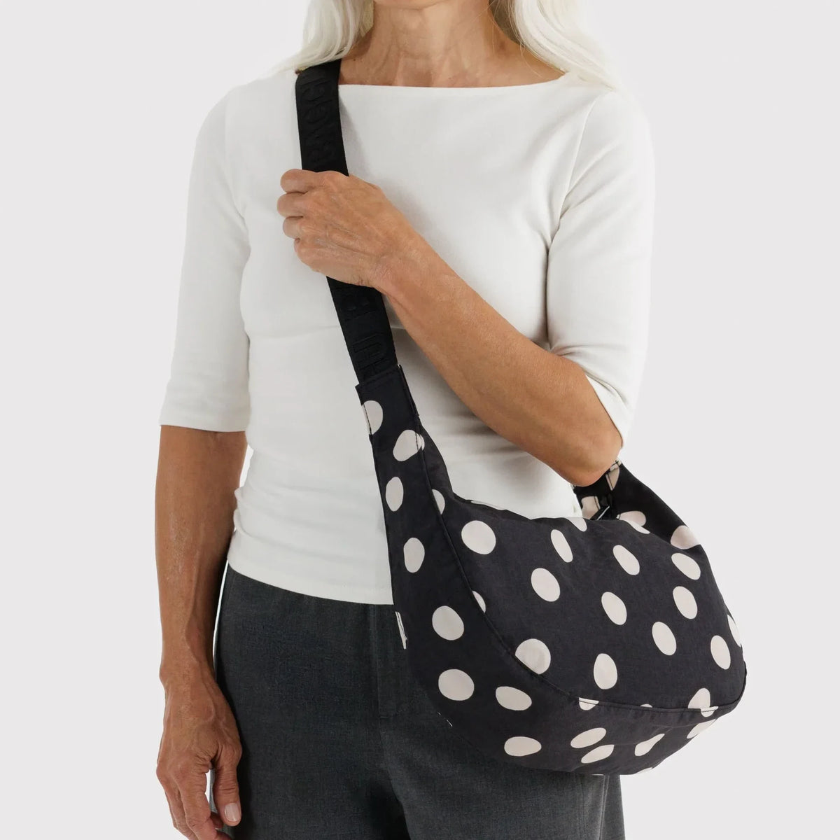 Medium crescent nylon bag with black-and-cream polka dots, worn crossbody over shoulder.