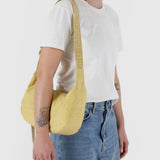 A person in a white T-shirt and blue jeans models a Baggu Medium Nylon Crescent Bag in butter-yellow, complete with the Baggu logo. This vibrant bag is machine washable, adding color to the outfit.