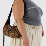 A person in a gray sleeveless top and beige skirt is holding a Baggu Medium Nylon Crescent Bag - Leopard.