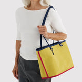 Reversible nylon tote bag with yellow lining and navy handles, carried