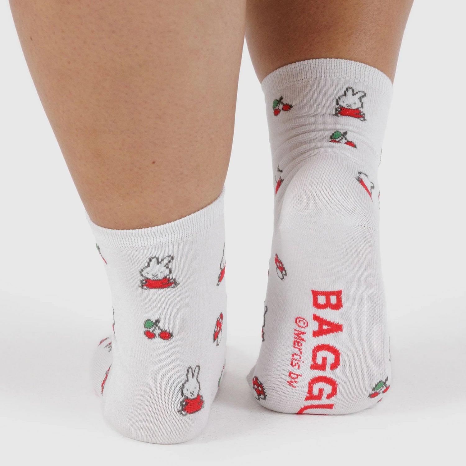 Close-up of feet in the Miffy x Baggu Crew Sock - White by Baggu, featuring small fruit and cartoon bunny designs with "BAGGU" and "Miffy" printed on the sole—perfect for fans of cute socks.