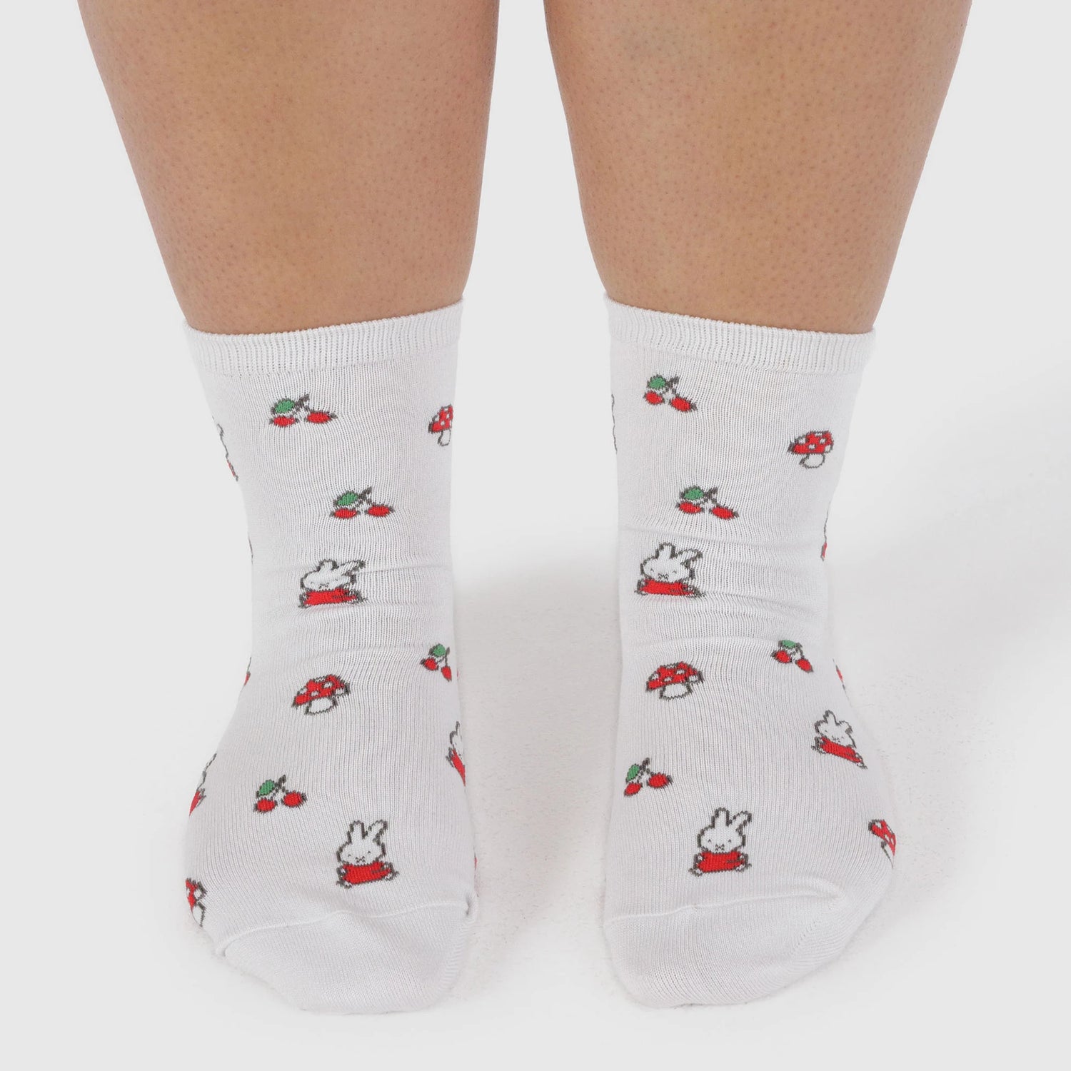 Two feet wearing Baggu’s Miffy x Baggu Crew Sock in white, featuring small printed cherries, mushrooms, and a cartoon bunny—perfect for Miffy socks fans.