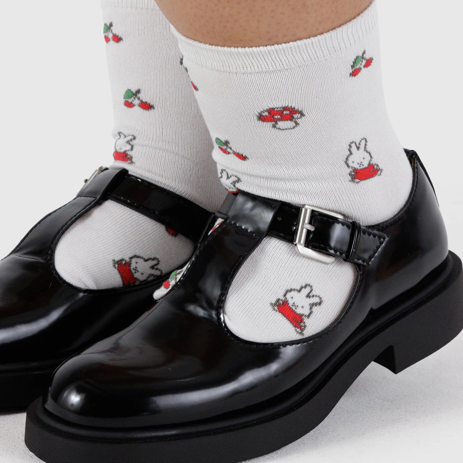 Person wearing Baggu Miffy x Baggu Crew Sock in white, featuring charming cartoon designs, paired with shiny black Mary Jane shoes on a light background.