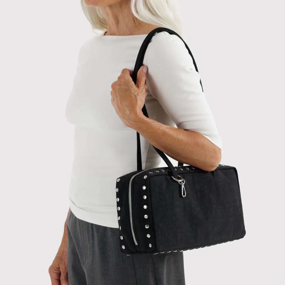 Black bowler bag with studded front zipper and two top handles, carried on shoulder