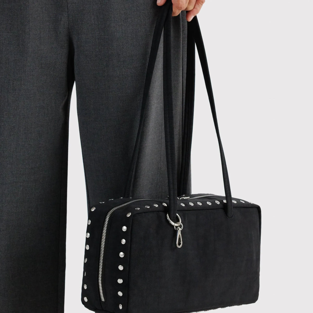 Black nylon bowler bag with side stud rows, front zipper pocket, held by handles