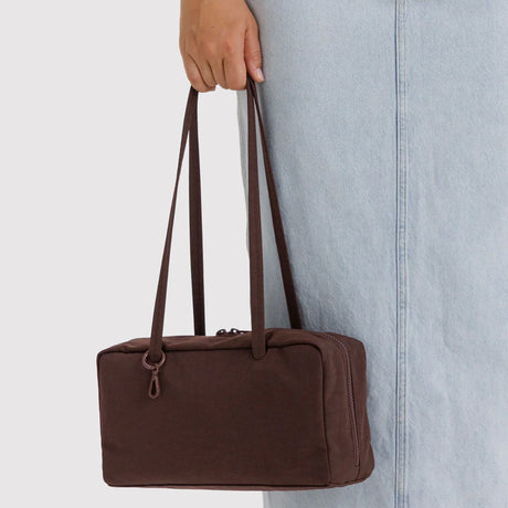 Rectangular dark brown fabric handbag with long slim handles held by person in light blue denim skirt