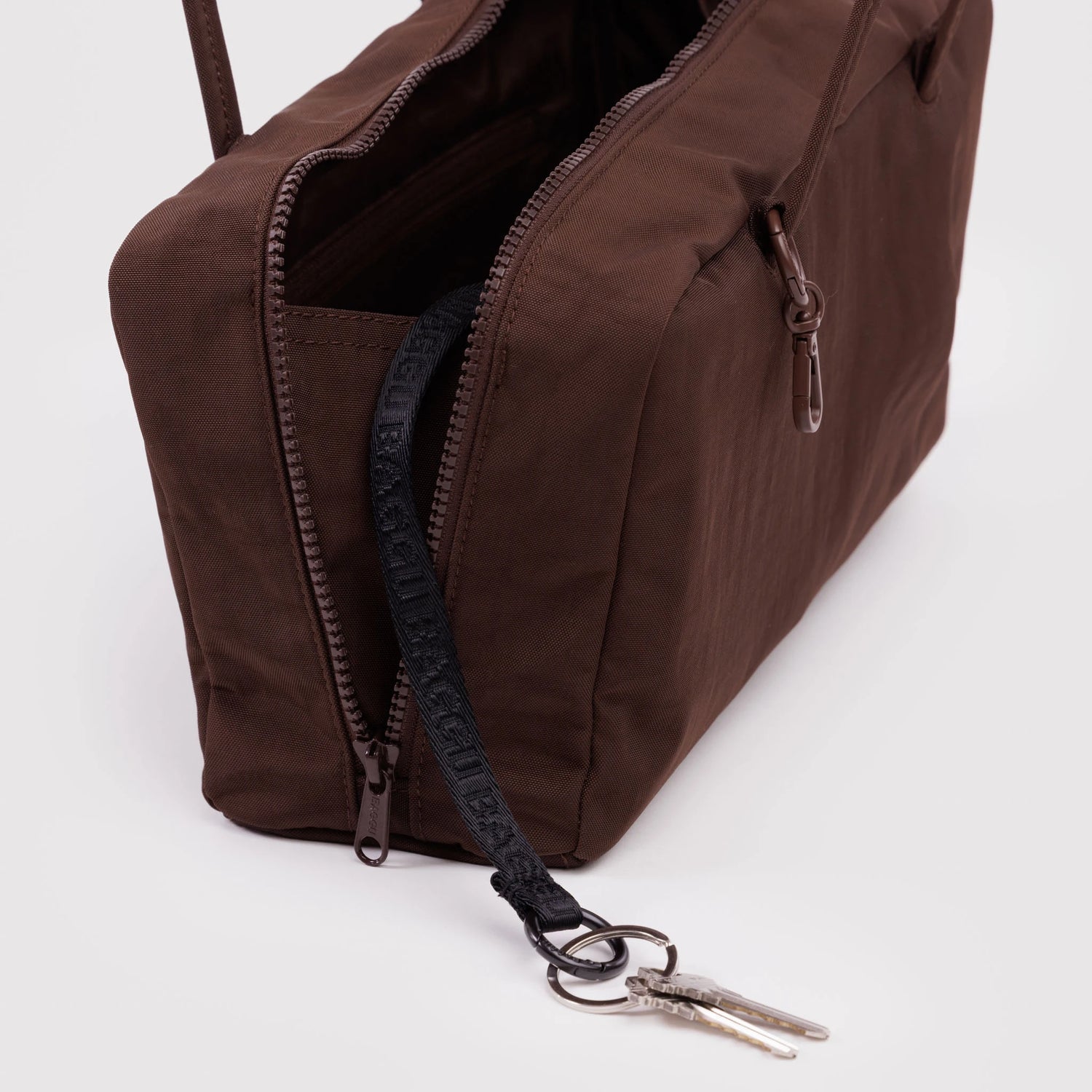 Brown rectangular fabric bag with dual zipper pockets and black key strap holding two silver keys