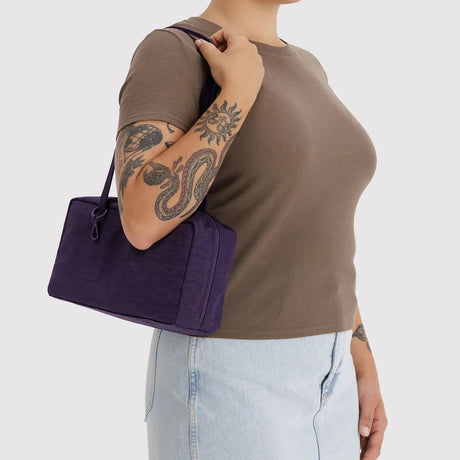 Person wearing brown short-sleeve top and light blue denim skirt carrying a rectangular deep purple handbag with short handles