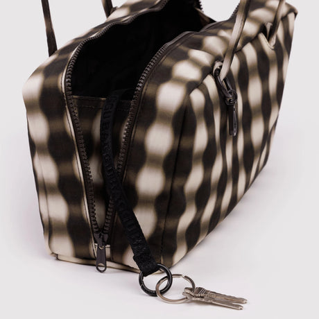 Rectangular shoulder bag with black and beige distorted checkered pattern, zipper open showing black interior and attached keyring with keys