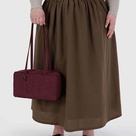 A person in a long brown skirt holds the Baggu Nylon Bowler Bag - Mahogany by Baggu, featuring two handles.