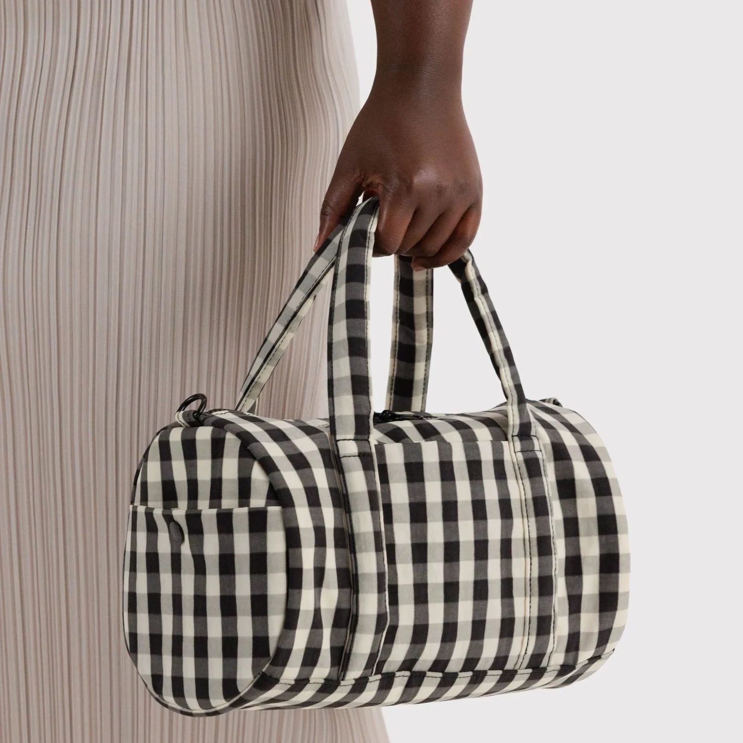 Nylon duffle bag in black-and-cream gingham, top handle held in hand