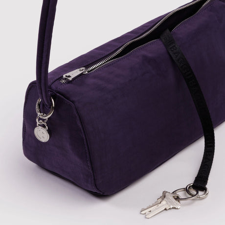 Slim deep purple fabric handbag with top zipper and round silver charm detail on white background